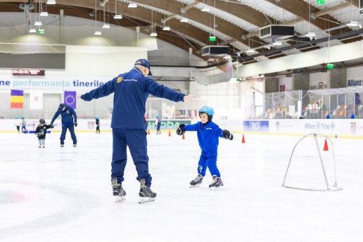 Antrenor îndrumând un copil la selecția de patinaj